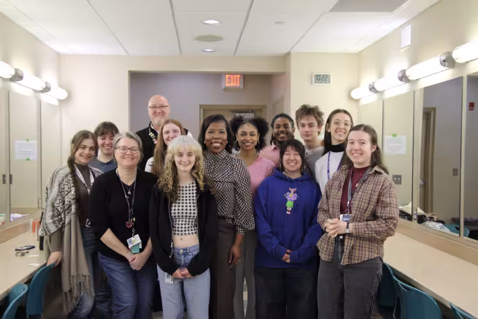 A group of students pose with their instructors in a theatre dressing room.