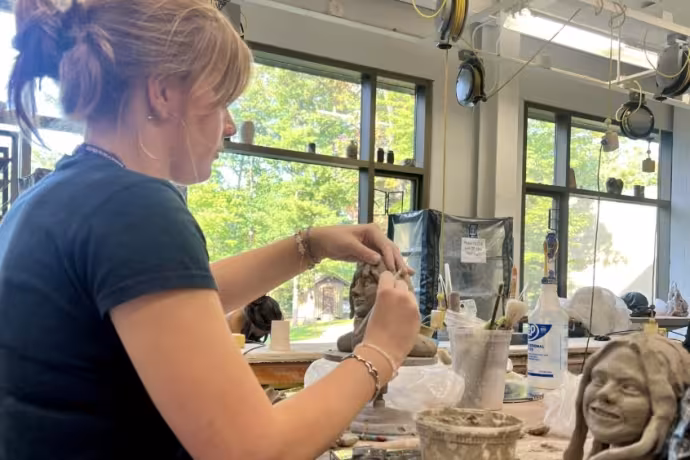 A student works with clay in a studio surrounded by trees.