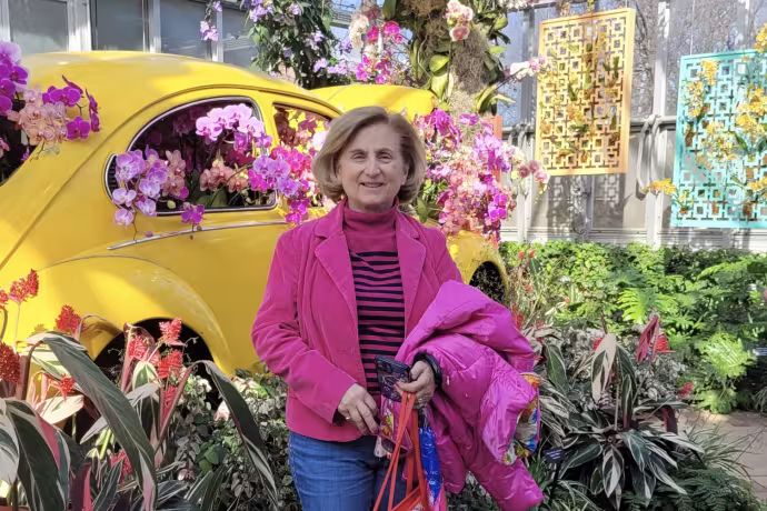 A woman dressed in bright pink poses next to a yellow car surrounded by flowers.