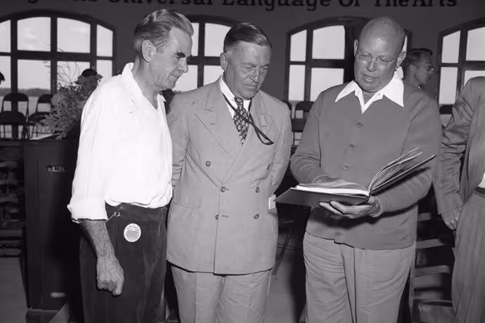 Three men gather around an open book of music.