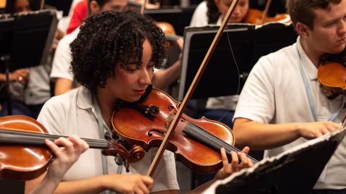 A violin student practices a piece alongside an orchestra 