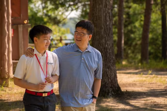 An arts camp student walks through campus with their parent