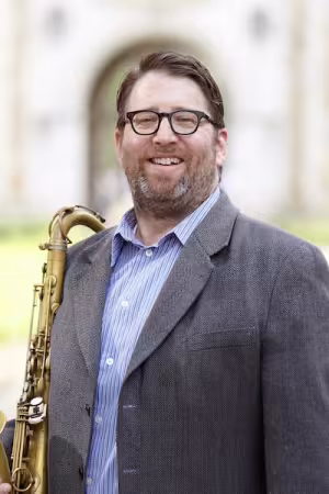 A saxophonist dressed in a gray suit smiles into the camera. 