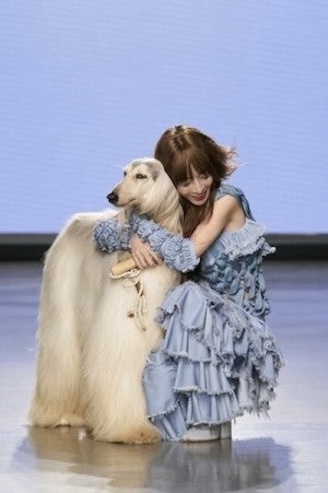 A fashion designer dressed in light blue pauses on the runway to hug her white-haired dog.