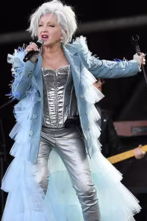 A musician wearing a creative blue and silver outfit sings passionately into the microphone.