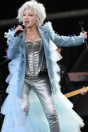 A musician wearing a creative blue and silver outfit sings passionately into the microphone.