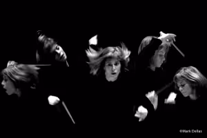 Black-and-white artistic composite portrait of conductor JoAnn Falletta in multiple motion-blurred poses against a dark background, capturing expressive gestures with baton and dynamic movement.