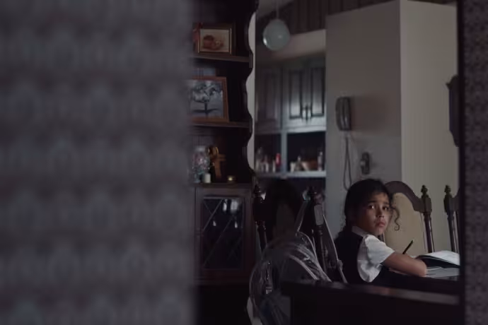 A young girl writing something at a table but is now looking afar