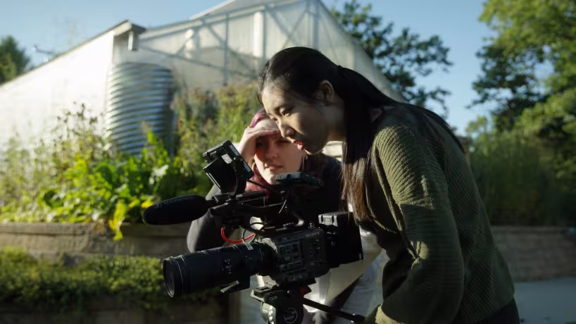 Grounded students film in front of greenhouse