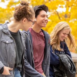 Three students walk across a fall campus