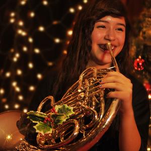A hornist poses in front of a Christmas tree
