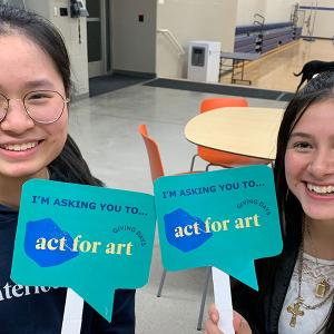 Two students hold signs reading 'I'm asking you to Act for Art'