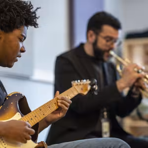 Two students playing music together. One is playing guitar, the other is playing trumpet. 