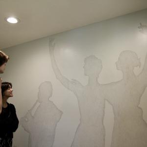 A group of people look at a light gray wall that has been decorated with the silhouettes of artists dancing and playing music.