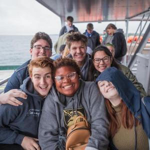 A group of six students smile at the camera from the deck of a ferry.