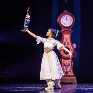 A young girl dressed in white holds up a nutcracker.