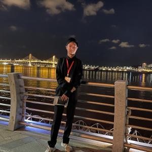 A student dressed in black leans against a bridge overlooking a cityscape at night.