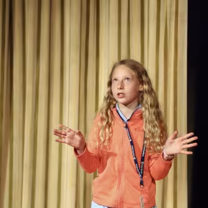 A young actor gestures expressively in front of a curtain.
