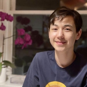 A student with short hair and dark eyes smiles into the camera near a pot of orchids.