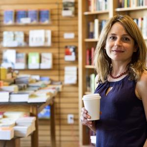 Author Karen Russell poses with a coffee in her hand as she stands in a bookstore.