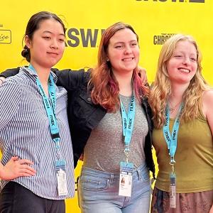 Three Film & New Media students pose in front of a yellow step-and-repeat.