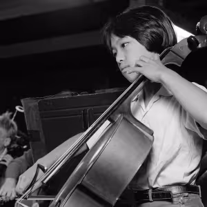 A child with short hair and wearing a light-colored shirt is deeply engaged in playing the as part of a children's orchestra. 