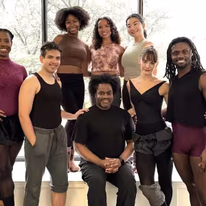 A group of dancers dressed in purple pose with their artistic director. 