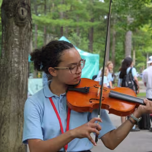 A young student plays a violin outdoors.