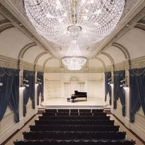 Shot of a stunning, chandelier-hung recital hall with a piano onstage.