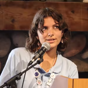 A creative writing student stands at a podium with a microphone, reading from a piece of paper.