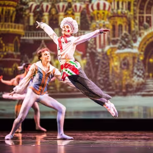 A young dancer dressed as a baker leaps into the air onstage.