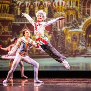 A young dancer dressed as a baker leaps into the air onstage.