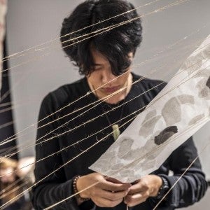 A visual arts student works on an installation with strings and paper.