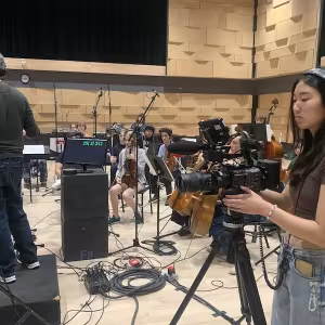 A student with a camera films as an orchestra plays.