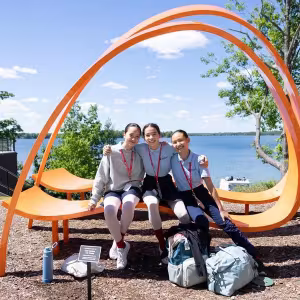 Three students relax on a creatively-designed orange bench