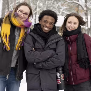 Three warmly-dressed students smile in the snow.