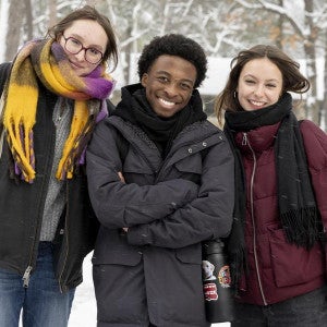 Three warmly-dressed students smile in the snow.