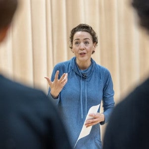 A voice coach gestures excitedly before an audience of students.