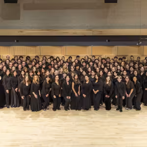 A group of students wearing black pose in a rehearsal room. 
