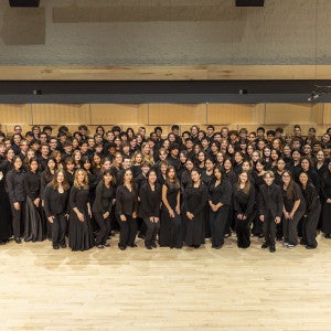 A group of students wearing black pose in a rehearsal room. 