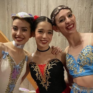 Three student dancers in colorful costumes hug each other and smile.