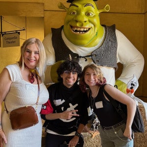 Two students pose witn an instructor in front of a life-size sculpture of Shrek.