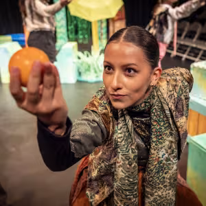 A student wearing a colorful scarf gazes excitedly at an orange in her hand.