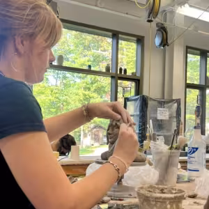 A student works with clay in a studio surrounded by trees.