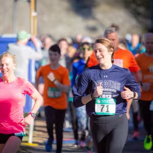 A group of runners in brightly-colored clothes nears the finish line of a race.