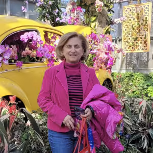 A woman dressed in bright pink poses next to a yellow car surrounded by flowers.