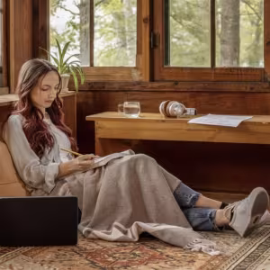 A young writer sits comfortably on the floor with a laptop and notebook.