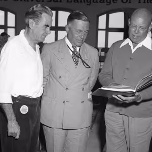 Three men gather around an open book of music.