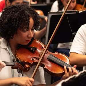 A violin student practices a piece alongside an orchestra 