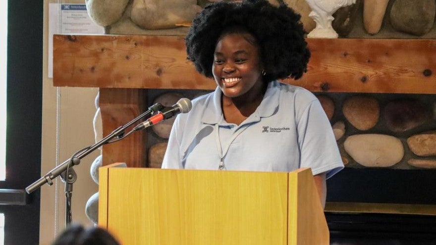 A smiling student wearing a blue polo stands at a podium.